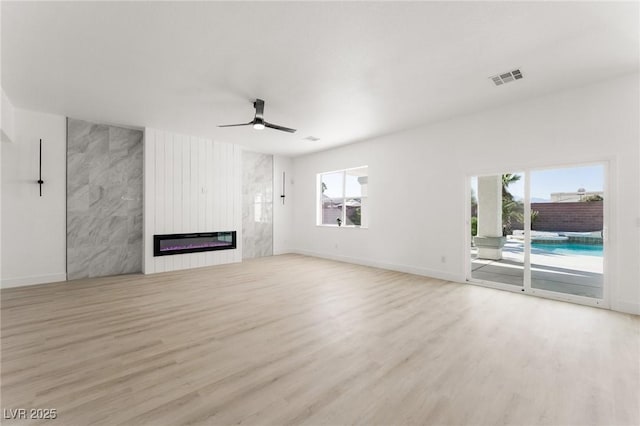 unfurnished living room featuring light hardwood / wood-style floors, a large fireplace, and ceiling fan