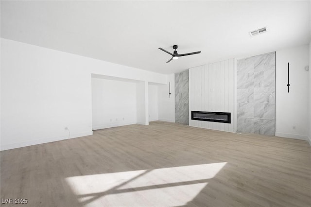 unfurnished living room with ceiling fan, a premium fireplace, and light wood-type flooring