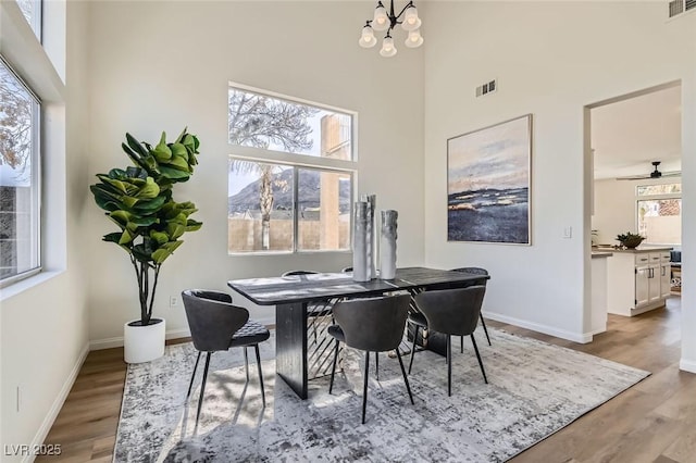 dining space with a notable chandelier, a towering ceiling, and light hardwood / wood-style flooring