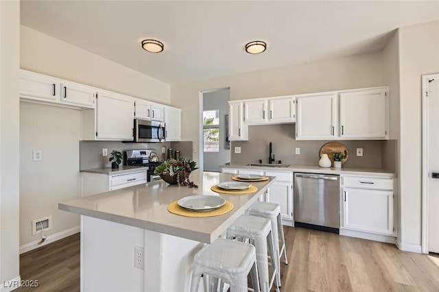 kitchen with a kitchen island, white cabinetry, sink, stainless steel appliances, and light wood-type flooring