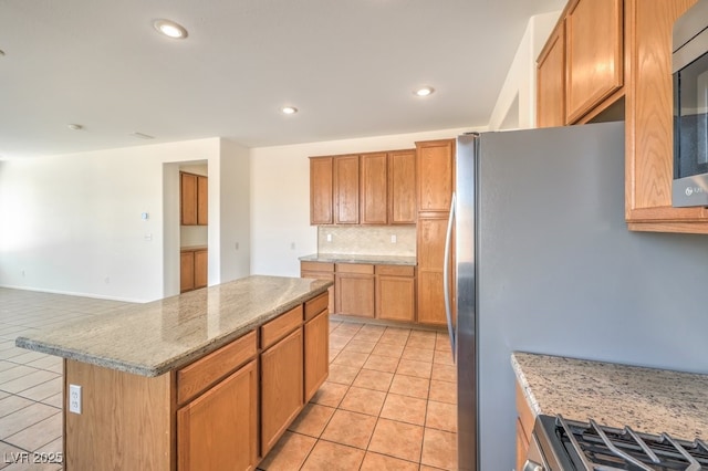 kitchen with light tile patterned flooring, appliances with stainless steel finishes, tasteful backsplash, a center island, and light stone counters