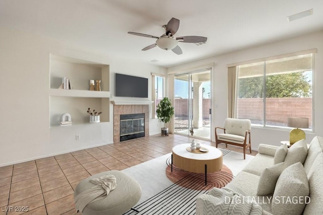 living room featuring a tiled fireplace, light tile patterned floors, built in features, and ceiling fan