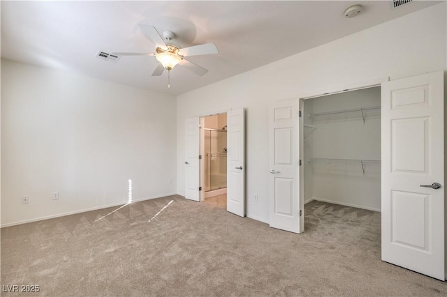 unfurnished bedroom featuring ensuite bath, a spacious closet, light colored carpet, a closet, and ceiling fan