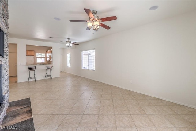 unfurnished living room with light tile patterned flooring, ceiling fan, and a stone fireplace