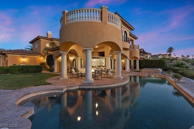 back house at dusk with a fenced in pool, a patio, and a balcony