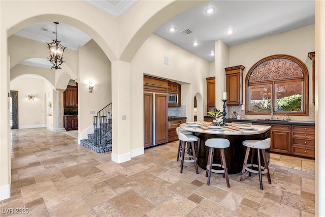 kitchen featuring a towering ceiling, tasteful backsplash, a center island, built in appliances, and a notable chandelier