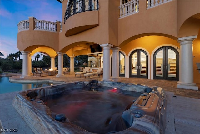 pool at dusk with french doors, an outdoor hot tub, and a patio area