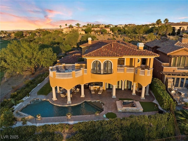 back house at dusk with a balcony, an outdoor fire pit, and a patio area