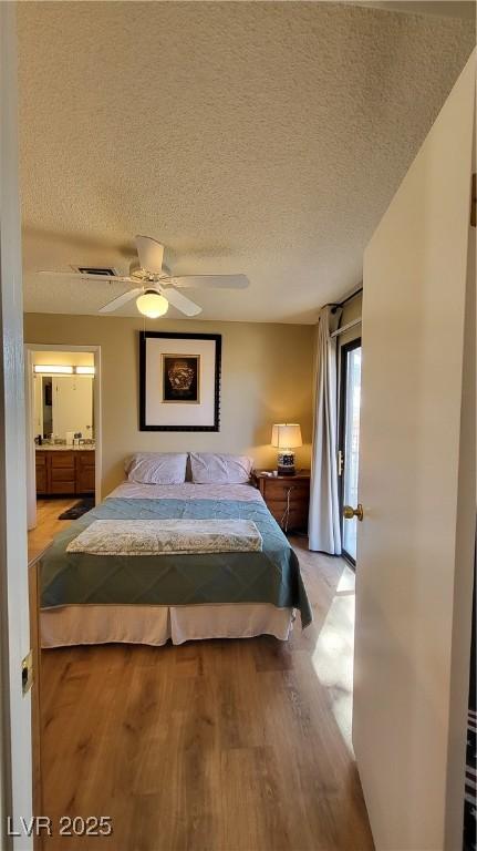 bedroom with ceiling fan, ensuite bath, light hardwood / wood-style floors, and a textured ceiling