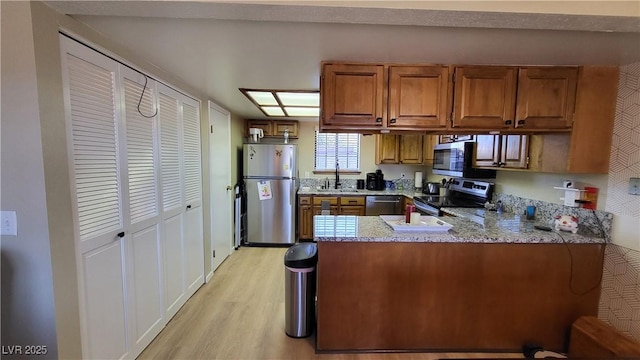 kitchen with sink, light hardwood / wood-style flooring, kitchen peninsula, stainless steel appliances, and light stone countertops