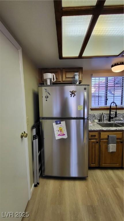 kitchen featuring light hardwood / wood-style flooring, sink, stainless steel fridge, and light stone countertops