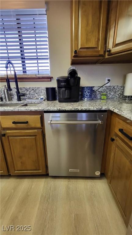 kitchen featuring dishwasher, sink, light stone counters, and light wood-type flooring