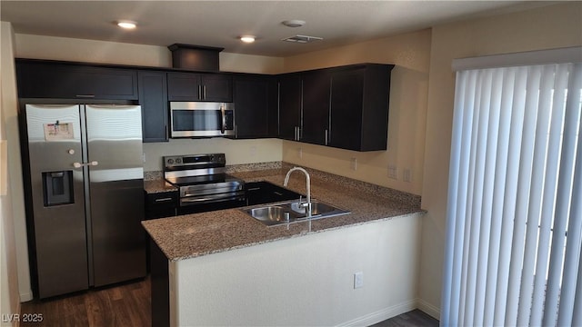 kitchen with appliances with stainless steel finishes, sink, light stone counters, kitchen peninsula, and dark wood-type flooring