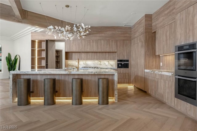 74 Innisbrook Ave, Las Vegas, NV 89113 - kitchen featuring light brown cabinets, stainless steel double oven, modern cabinets, a center island with sink, and a notable chandelier