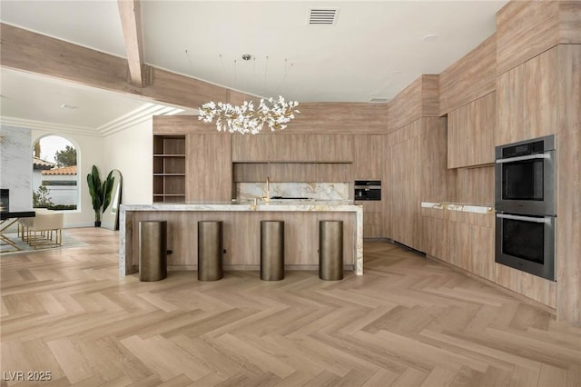 kitchen with double oven, a breakfast bar area, a chandelier, a large island, and light parquet flooring