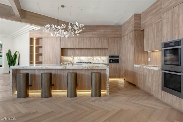 kitchen featuring double oven, an island with sink, light parquet flooring, and a kitchen bar