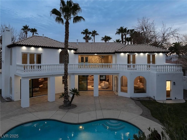 back house at dusk featuring a balcony and a patio area