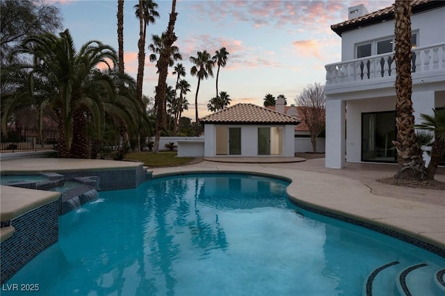 pool at dusk with an outdoor structure and a patio