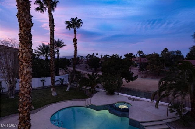 pool at dusk featuring an in ground hot tub and a patio