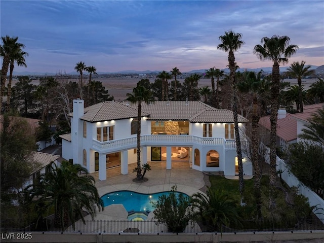 back house at dusk with a balcony and a patio