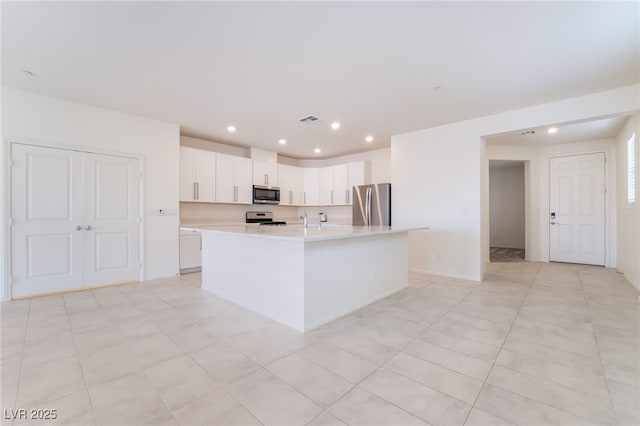 kitchen featuring a center island with sink, white cabinetry, stainless steel appliances, and light countertops