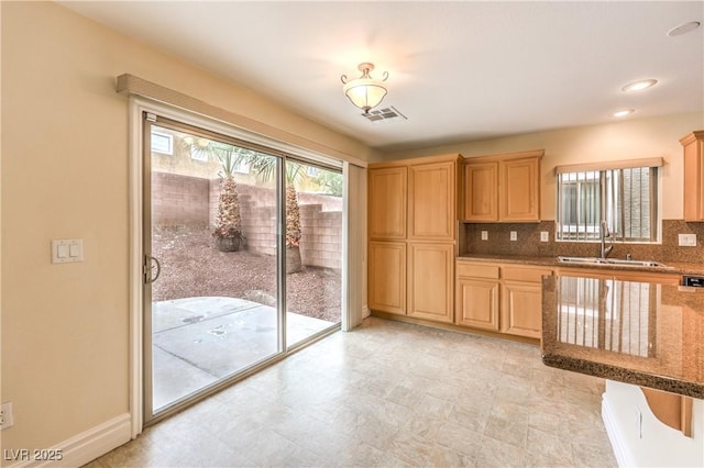 kitchen featuring tasteful backsplash, stone countertops, visible vents, light brown cabinets, and a sink