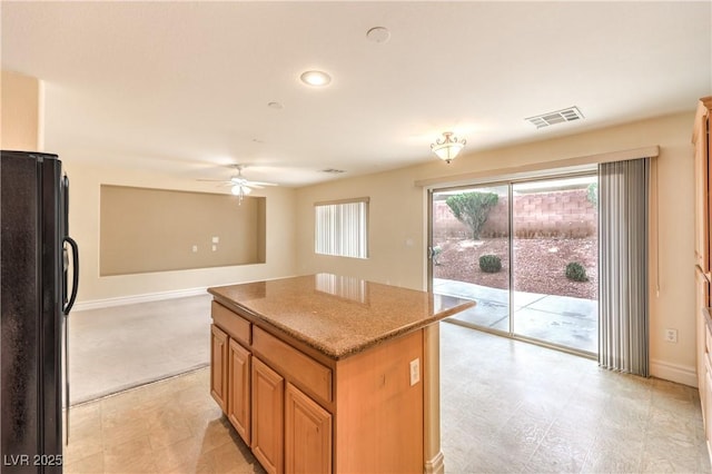 kitchen with light stone counters, a kitchen island, visible vents, baseboards, and freestanding refrigerator