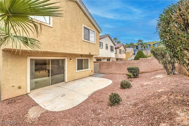 rear view of house with a patio area, fence, and stucco siding