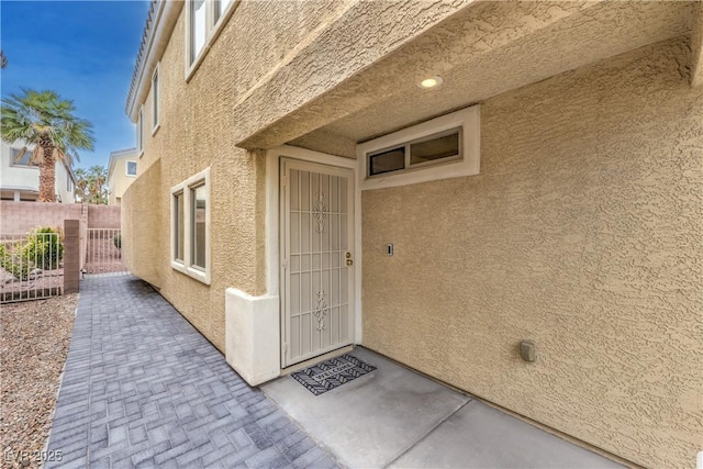 view of exterior entry with fence and stucco siding