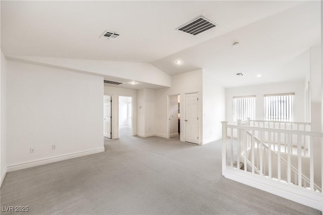 spare room featuring vaulted ceiling, light colored carpet, visible vents, and baseboards