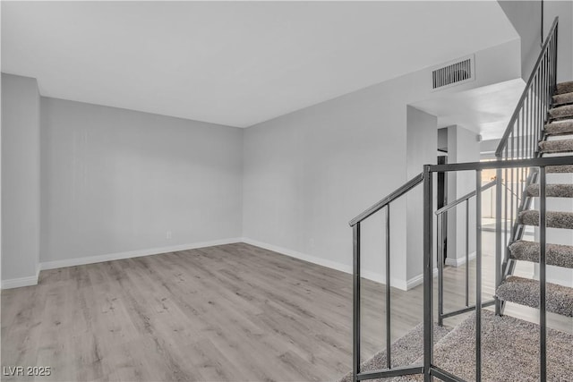 unfurnished room featuring light wood-style flooring, stairway, visible vents, and baseboards