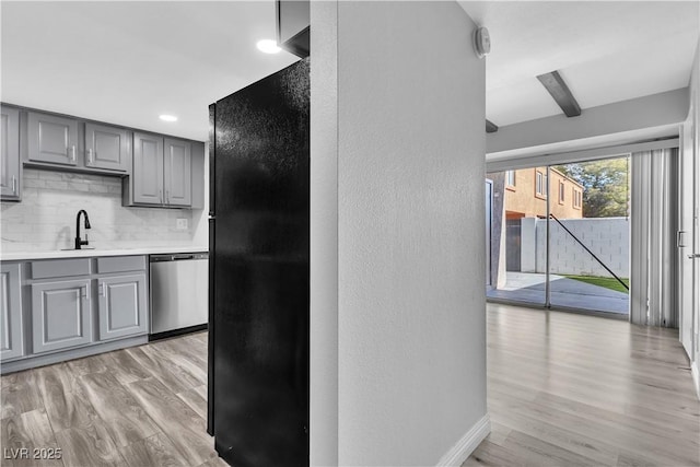 kitchen with a sink, light countertops, stainless steel dishwasher, freestanding refrigerator, and decorative backsplash