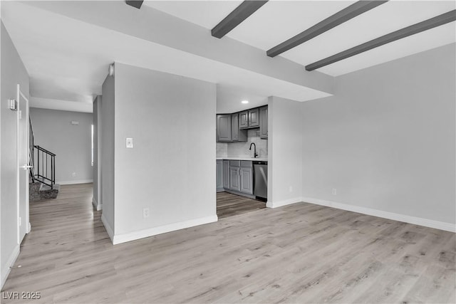 unfurnished living room featuring beam ceiling, stairway, light wood-style floors, a sink, and baseboards