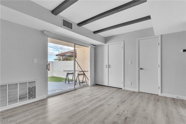 interior space with beam ceiling, light wood-style flooring, visible vents, and baseboards