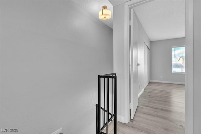 hall featuring light wood-style flooring, baseboards, and a textured ceiling