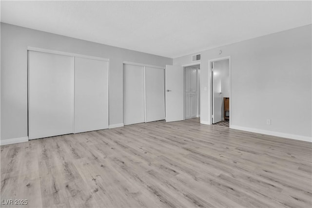 unfurnished bedroom with light wood-type flooring, baseboards, visible vents, and multiple closets