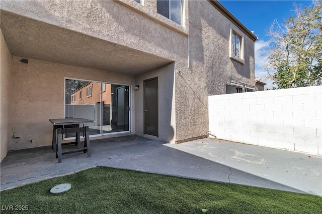 view of exterior entry featuring a patio, fence, and stucco siding