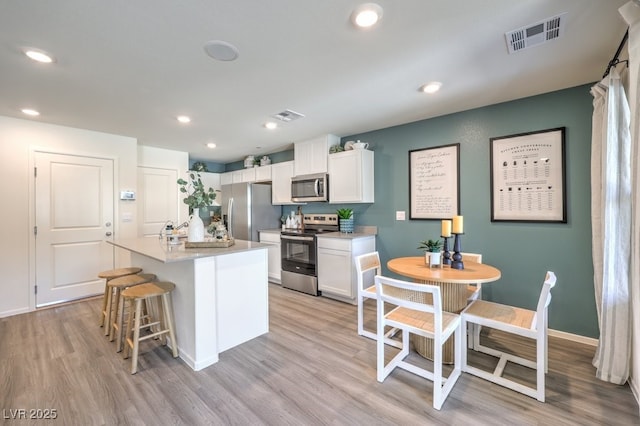 kitchen with a kitchen island with sink, light hardwood / wood-style flooring, stainless steel appliances, and white cabinets