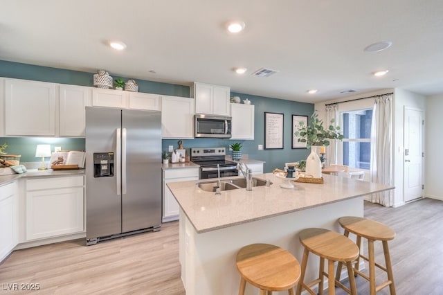 kitchen with stainless steel appliances, an island with sink, white cabinets, and light stone counters