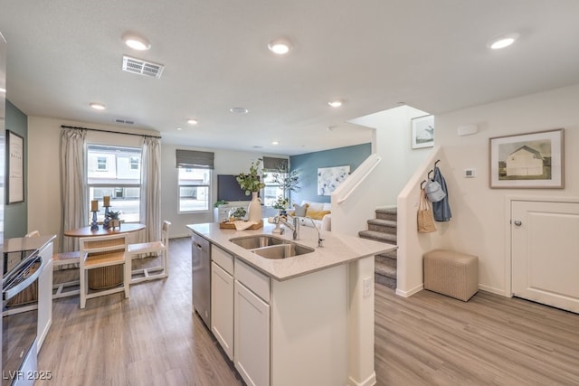 kitchen with sink, dishwasher, light hardwood / wood-style floors, an island with sink, and white cabinets