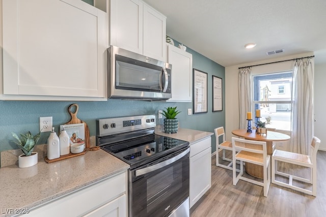 kitchen with white cabinetry, stainless steel appliances, light stone countertops, and light hardwood / wood-style flooring