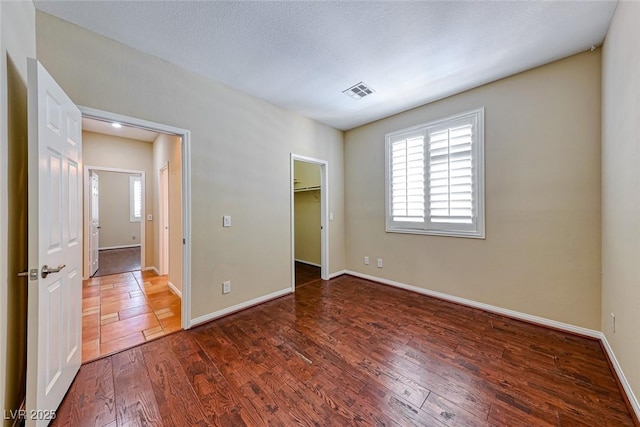 unfurnished bedroom featuring a walk in closet, visible vents, dark wood finished floors, and baseboards