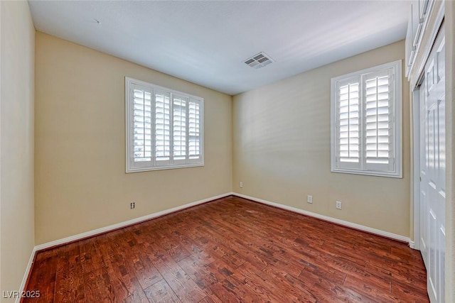 spare room with dark wood-style floors, visible vents, and baseboards