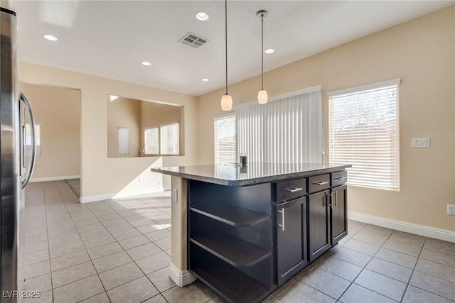 kitchen featuring stainless steel refrigerator, a center island, light tile patterned flooring, decorative light fixtures, and dark stone counters