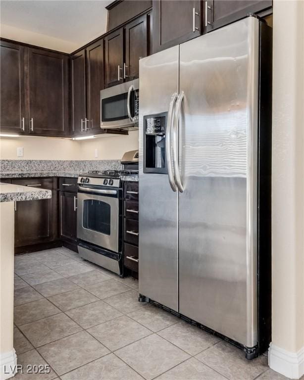 kitchen featuring stainless steel appliances, light tile patterned flooring, dark brown cabinets, and light stone counters