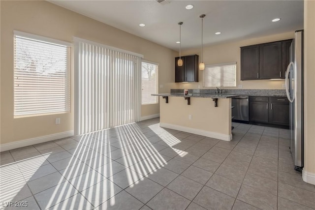 kitchen with light tile patterned floors, hanging light fixtures, stainless steel appliances, a kitchen breakfast bar, and a kitchen island