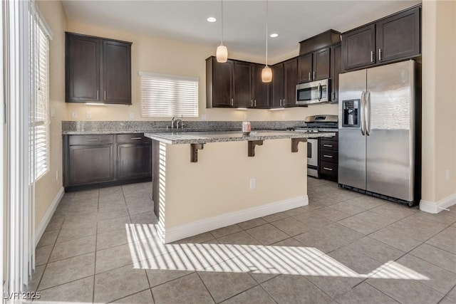 kitchen with a breakfast bar, stainless steel appliances, a center island, light stone countertops, and decorative light fixtures