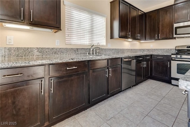 kitchen with sink, light tile patterned floors, stainless steel appliances, light stone counters, and dark brown cabinetry