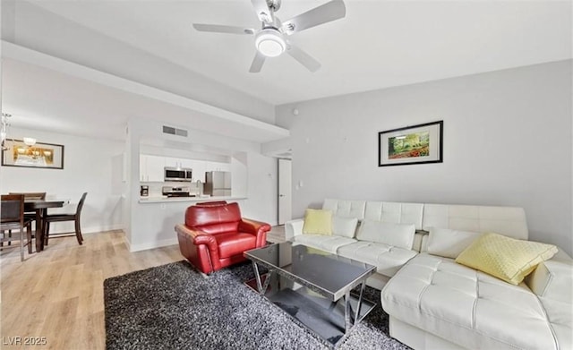 living room featuring ceiling fan with notable chandelier and light wood-type flooring