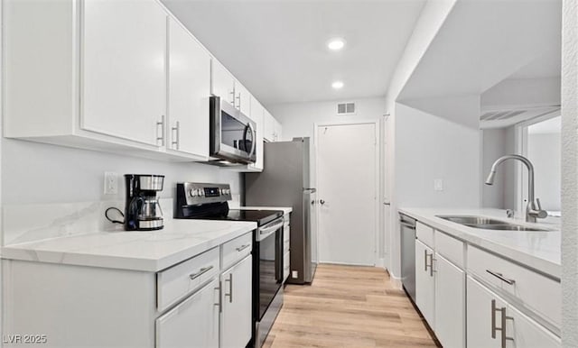 kitchen featuring stainless steel appliances, light stone countertops, sink, and white cabinets